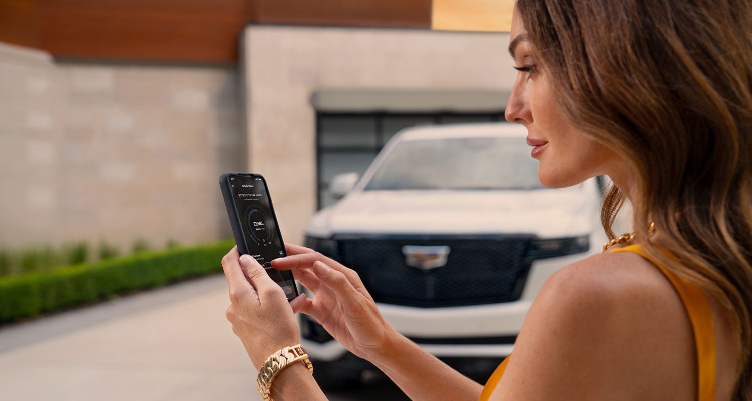 lady checking her mobile with a Cadillac vehicle background | Service Cadillac in Lafayette LA