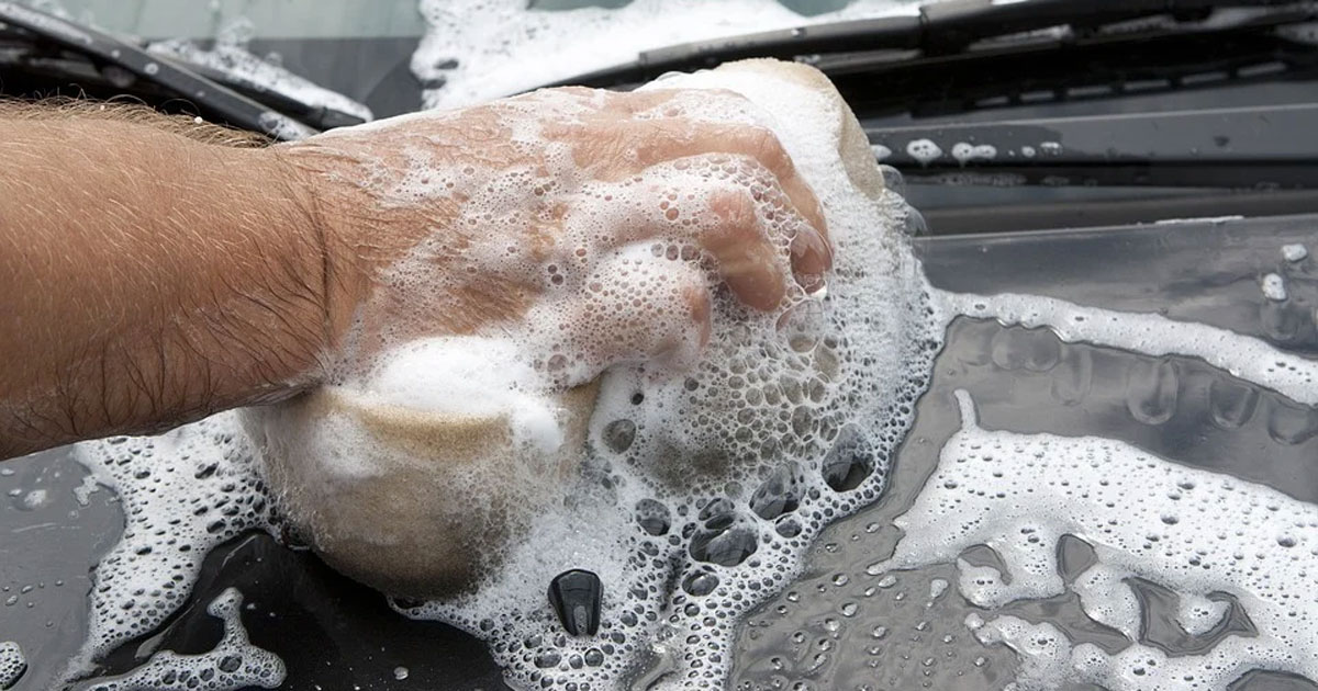 a hand holding a soapy sponge washing a black car