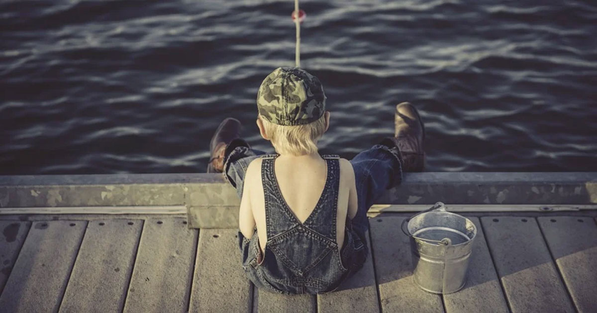 a small bow in overalls and a camo hat fishing off a pier