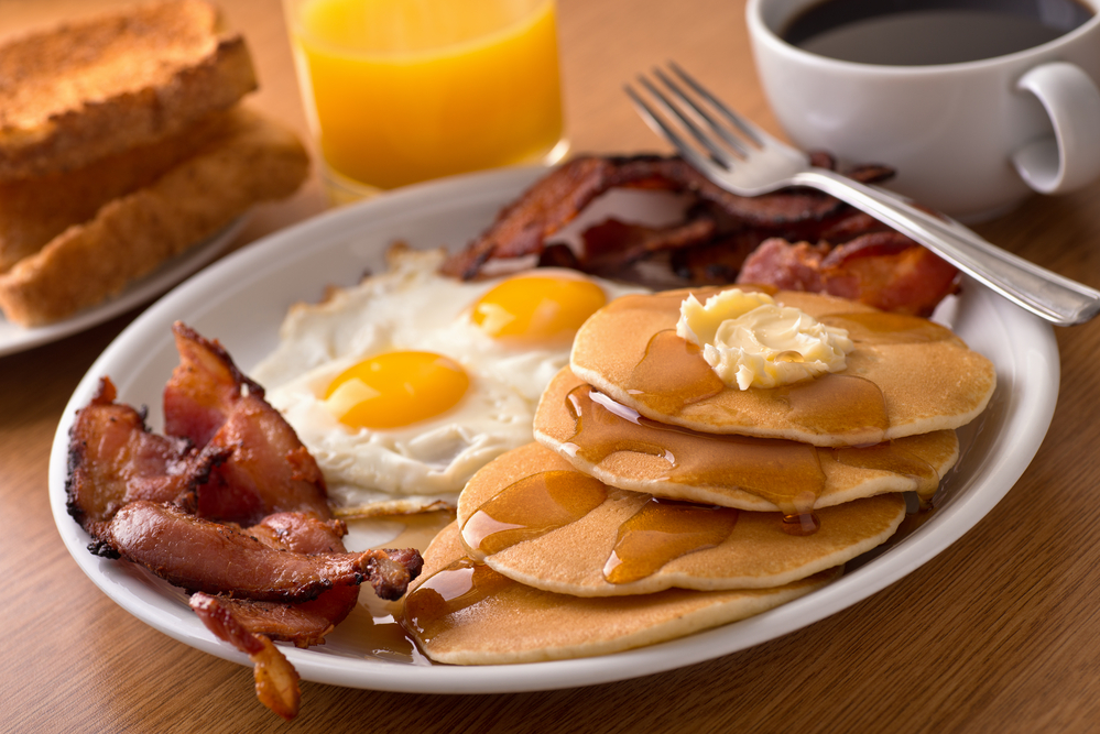 a plate with pancakes, bacon, and eggs with coffee and orange juice on the side.