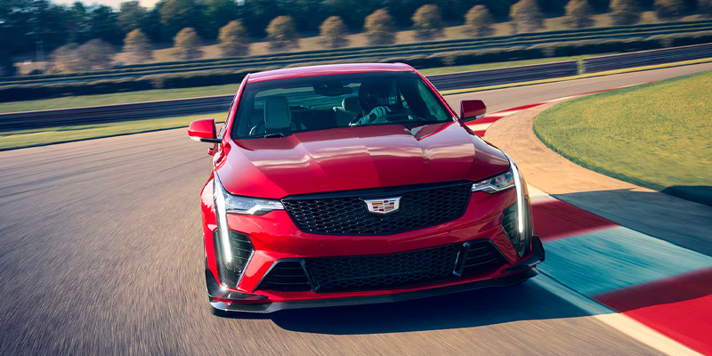 Red 2026 Cadillac CT4 V-Series sedan driving on a racetrack in Lafayette, LA, featuring a sporty design, aggressive front grille, and sharp LED lighting as it corners at speed.