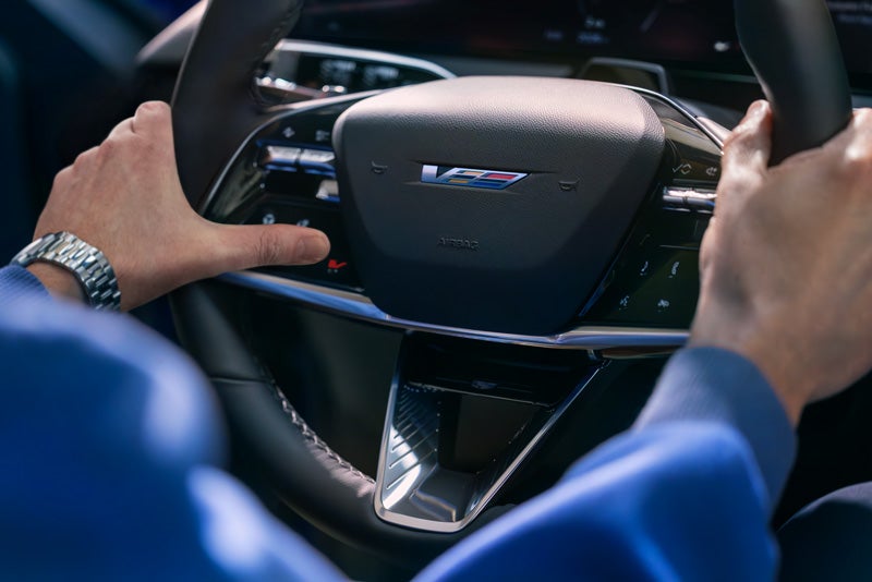Close-up of a Man About to Press the V-Button on the 2026 OPTIQ-V Steering Wheel | Service Cadillac in Lafayette LA